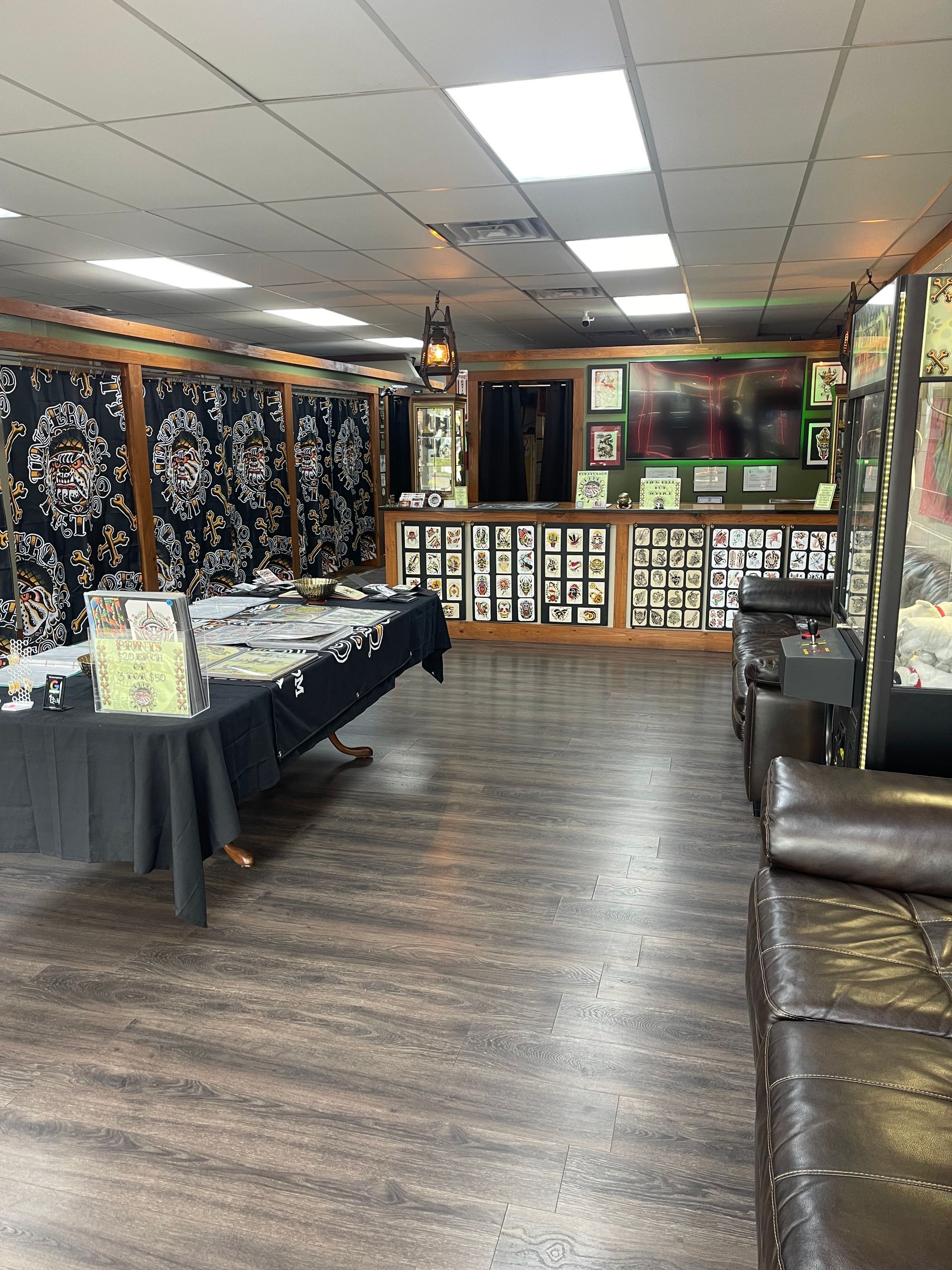 Tattoo studio interior with black tables, wall art, and brown leather seating in a dim room
