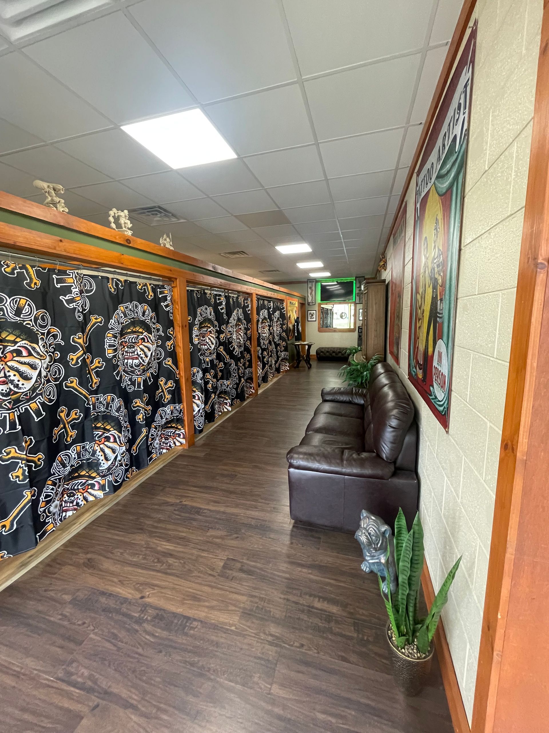 Long hallway with patterned curtains, brown leather seating, and plants under fluorescent ceiling lights.