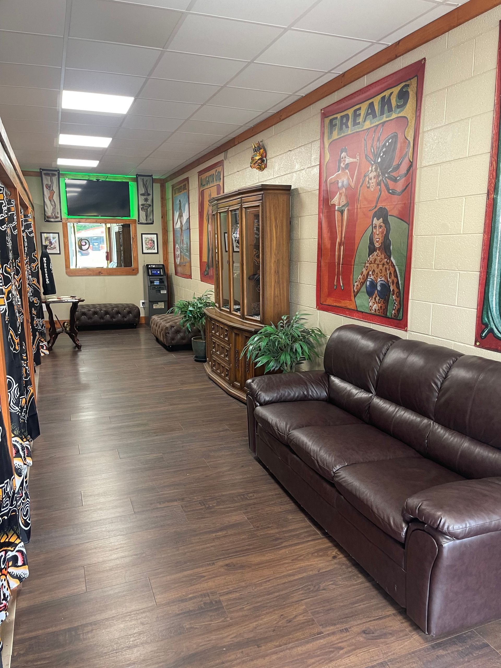 Narrow waiting room with brown leather couch, wood floors, potted plants, and framed posters along the wall.
