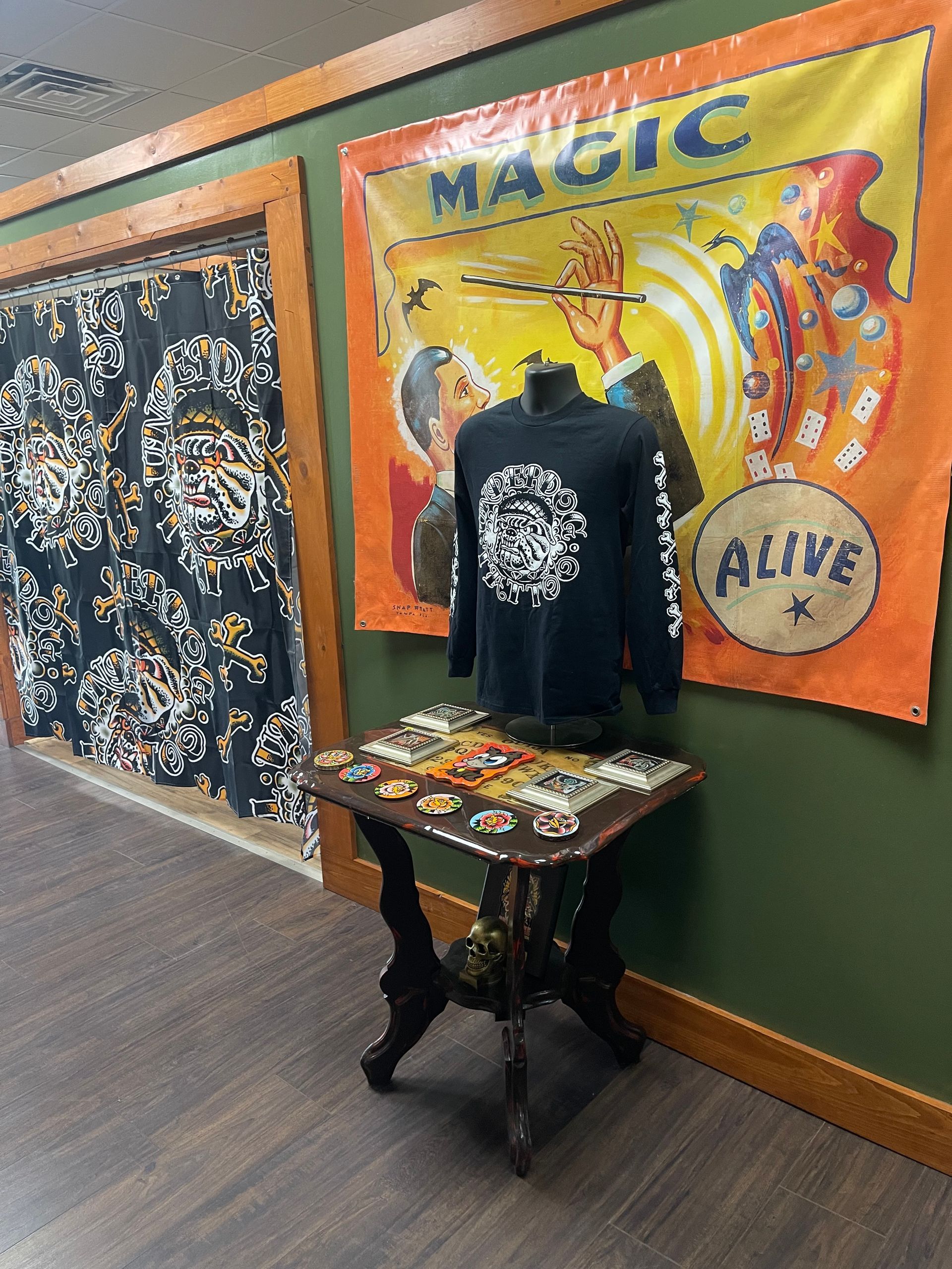 T-shirt display in a green-walled hallway with a colorful “Magic” banner and patterned backdrop.