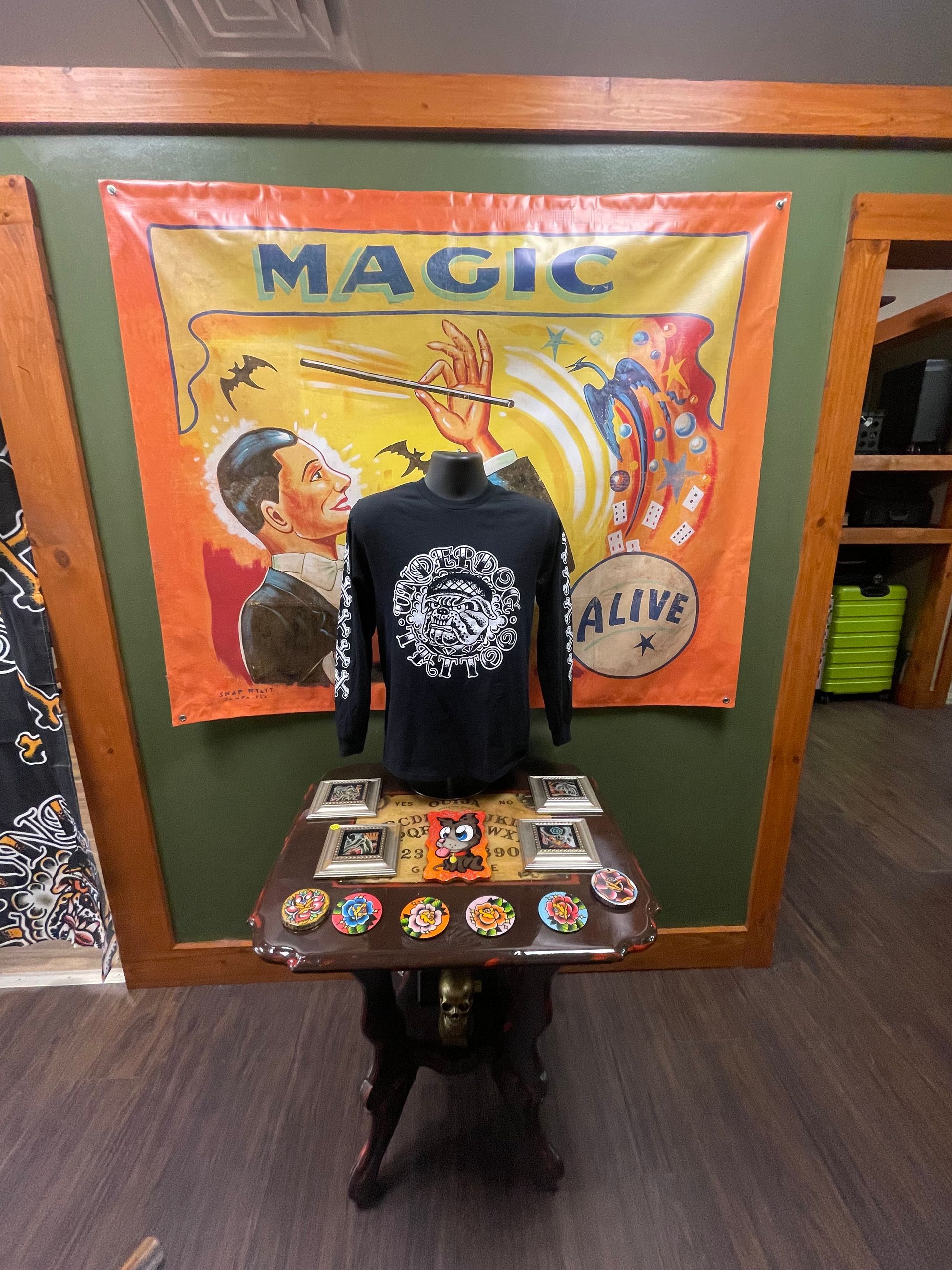 Magic-themed display with a black shirt, colorful banner, and table of patches in a shop.