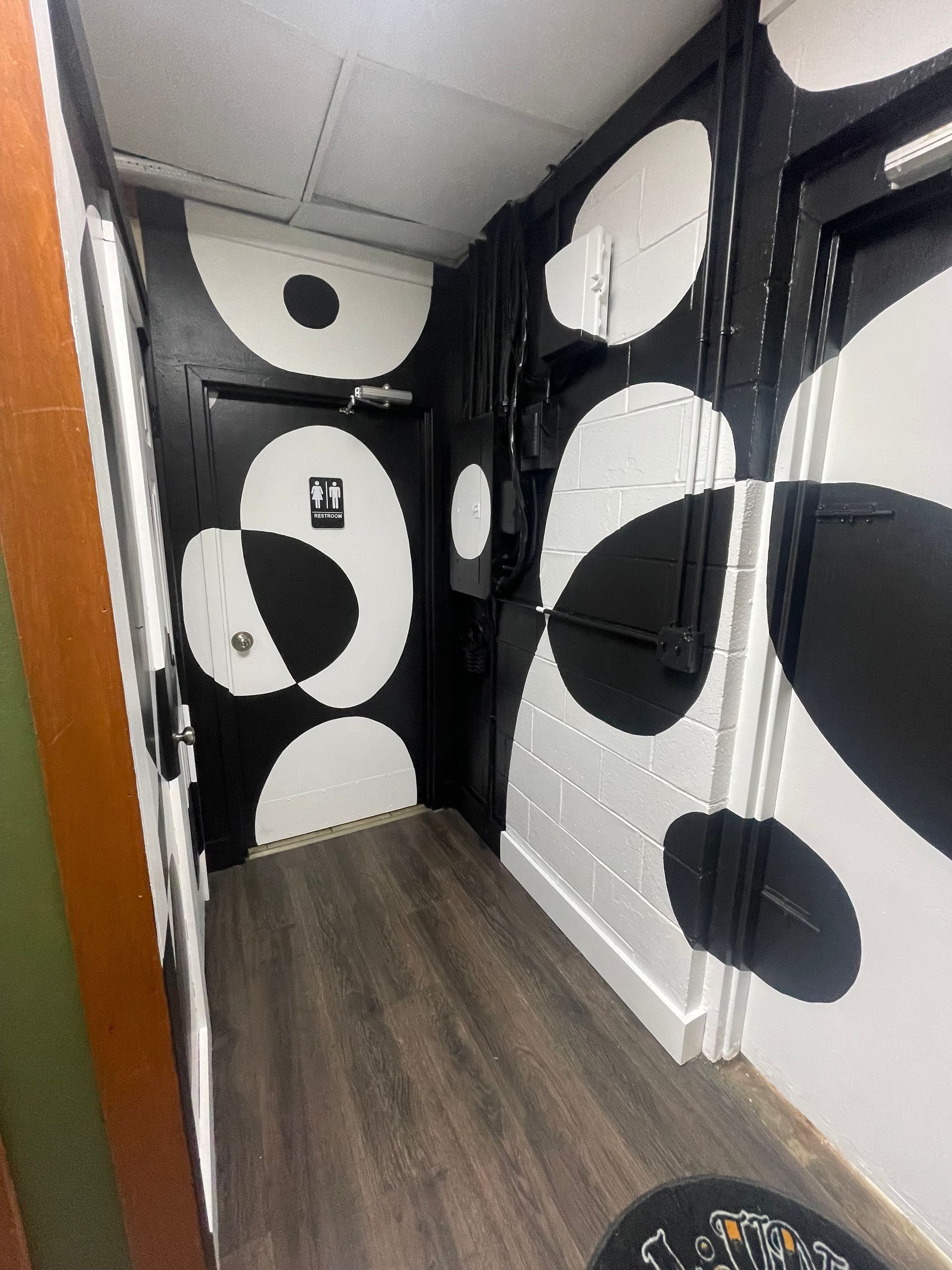Small room with black-and-white cow-print walls, wood floor, and a door at left.