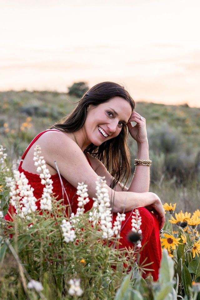 Woman in a red dress smiling in a wildflower field at sunset