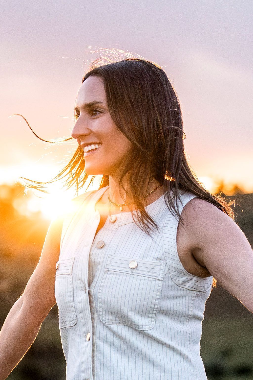 Woman in a white sleeveless dress smiling in sunset light outdoors