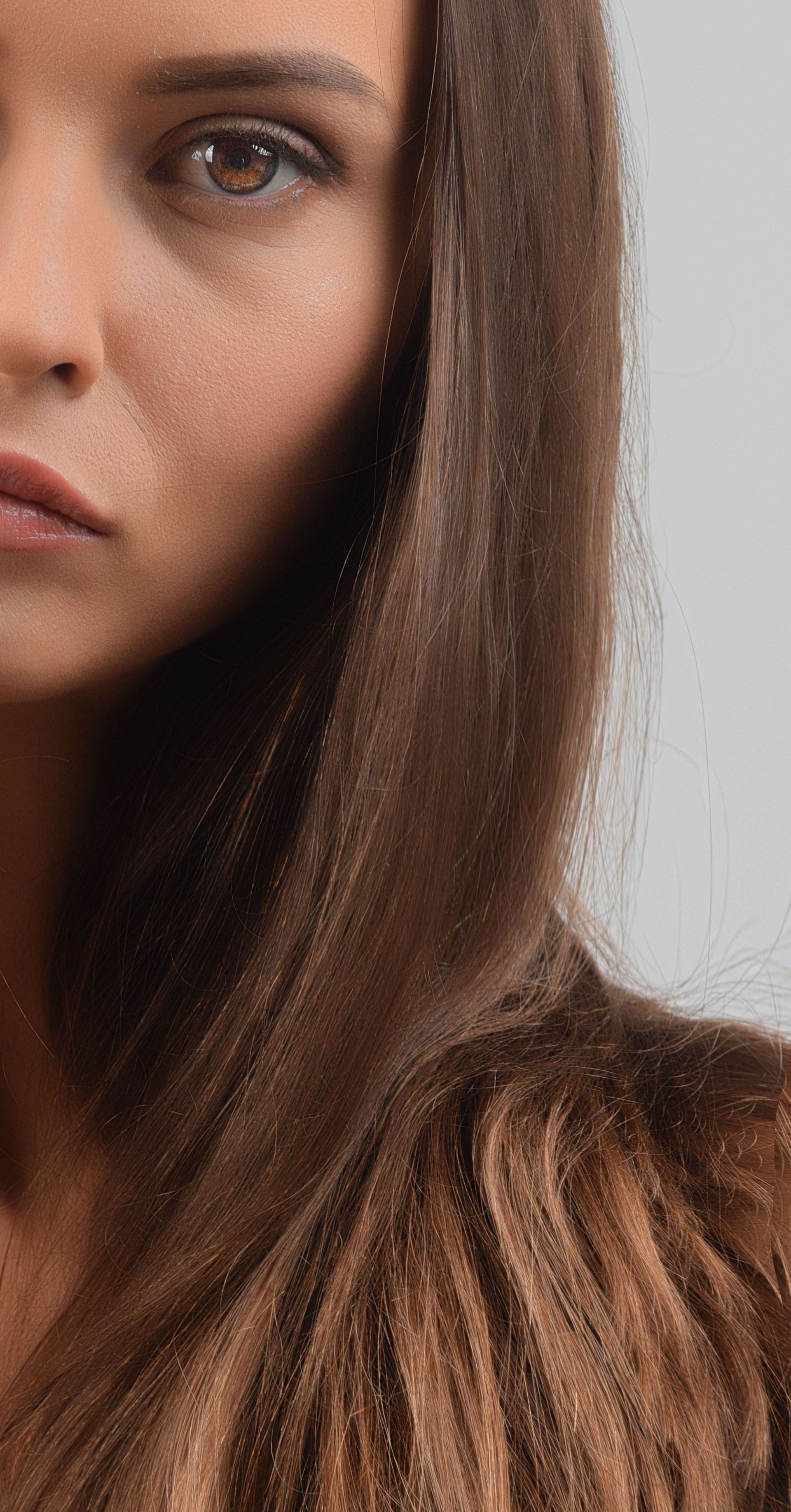 Close-up of a woman’s face with long brown hair against a light gray background