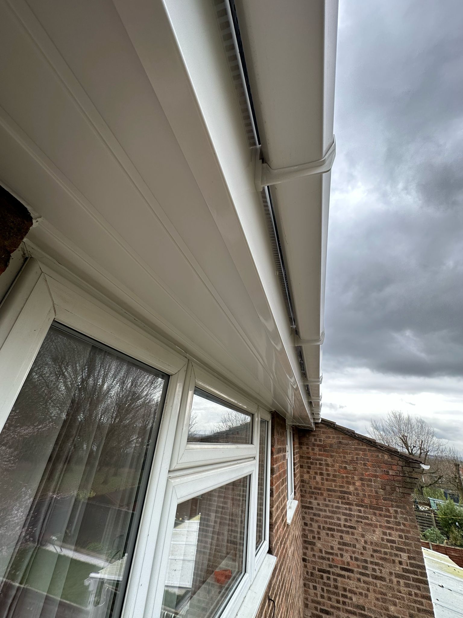 White eaves and guttering against a cloudy sky, above a window and brick building.