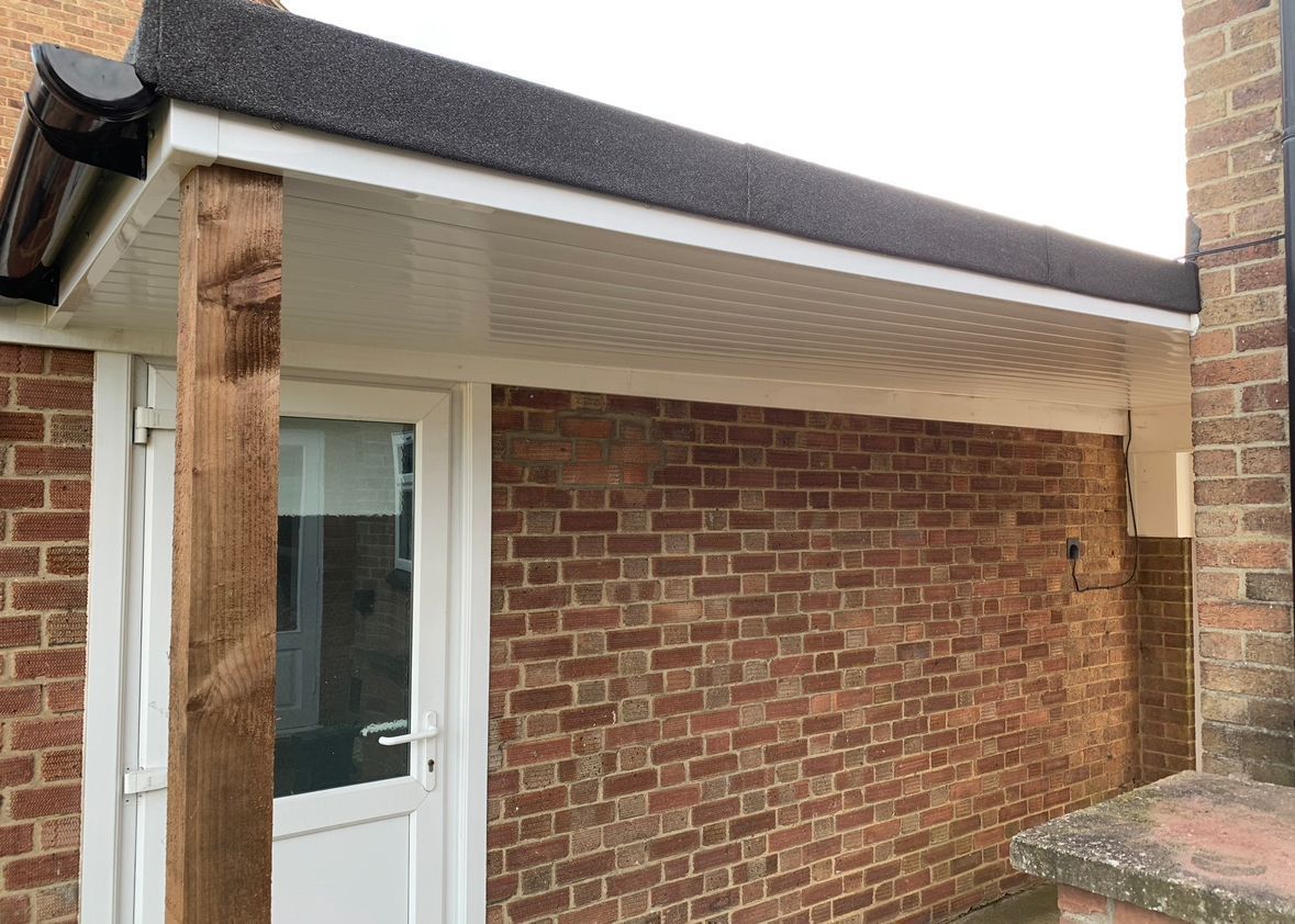 Brick building with white door, wood support, and flat roof with black trim and white paneling.