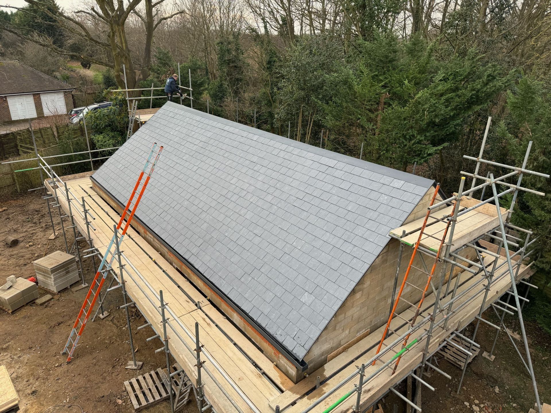 A partially constructed building with scaffolding, featuring a gray tiled roof.