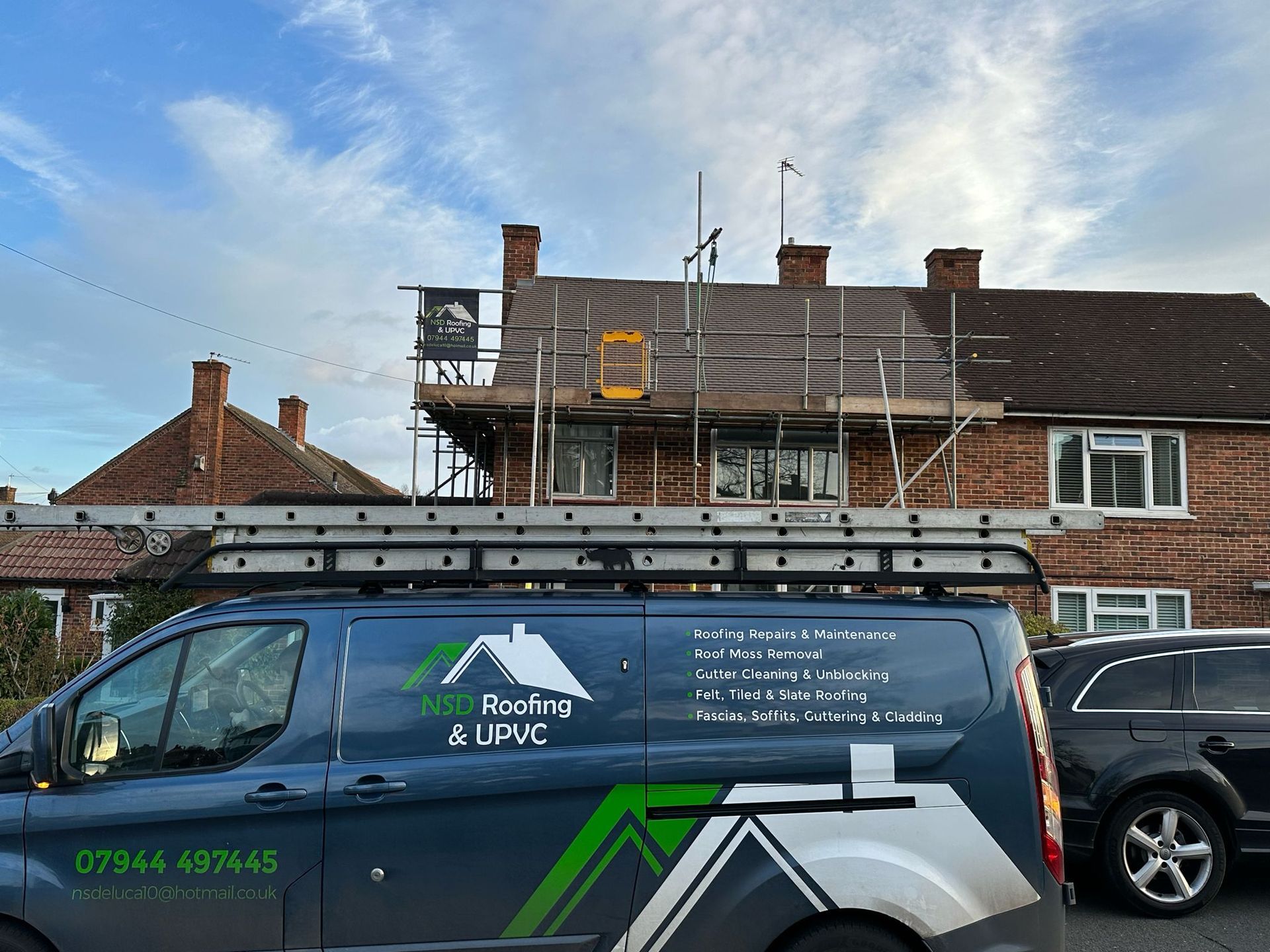 Blue van with roofing company logo parked in front of a house with scaffolding on the roof.