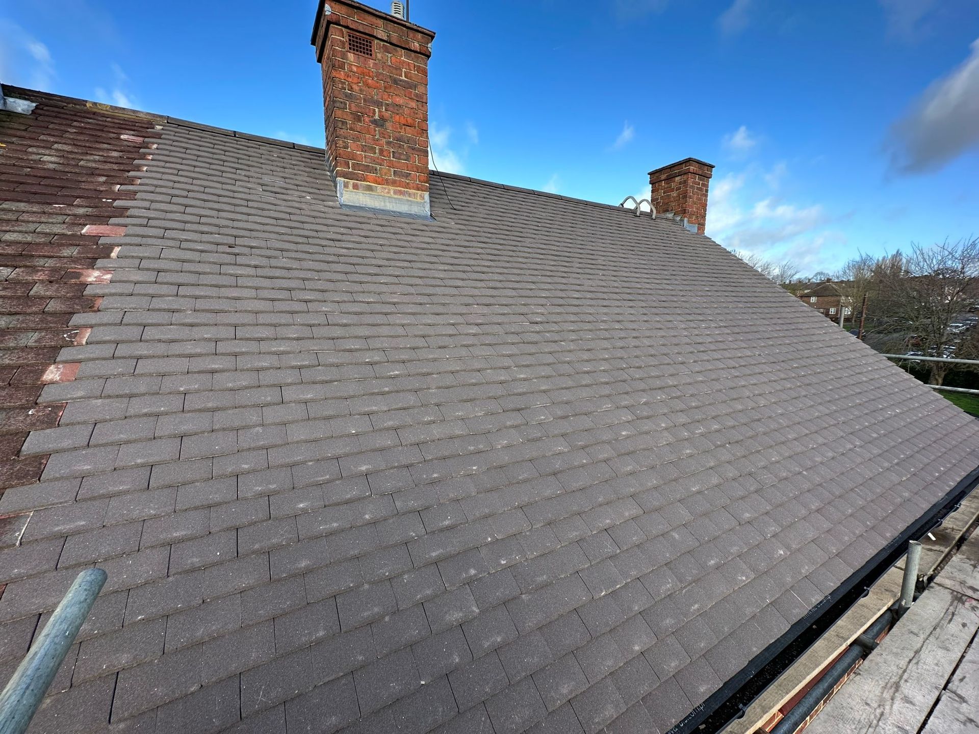 A rooftop with dark gray shingles, two brick chimneys, and a clear blue sky.