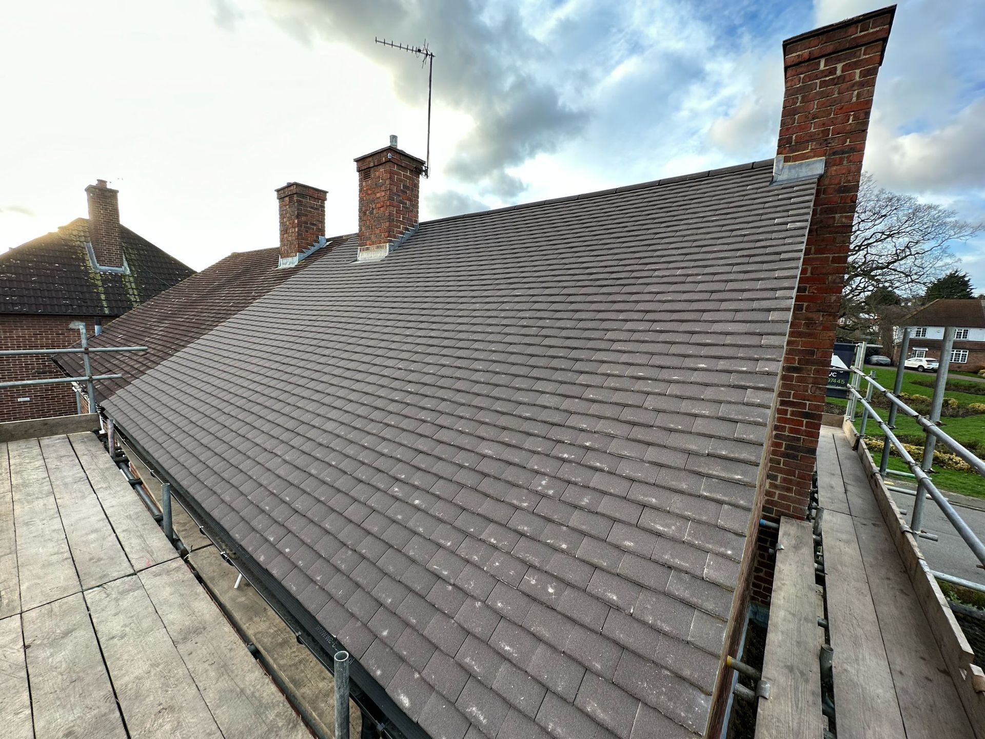 A roof with gray tiles, scaffolding, brick chimneys against a cloudy sky.