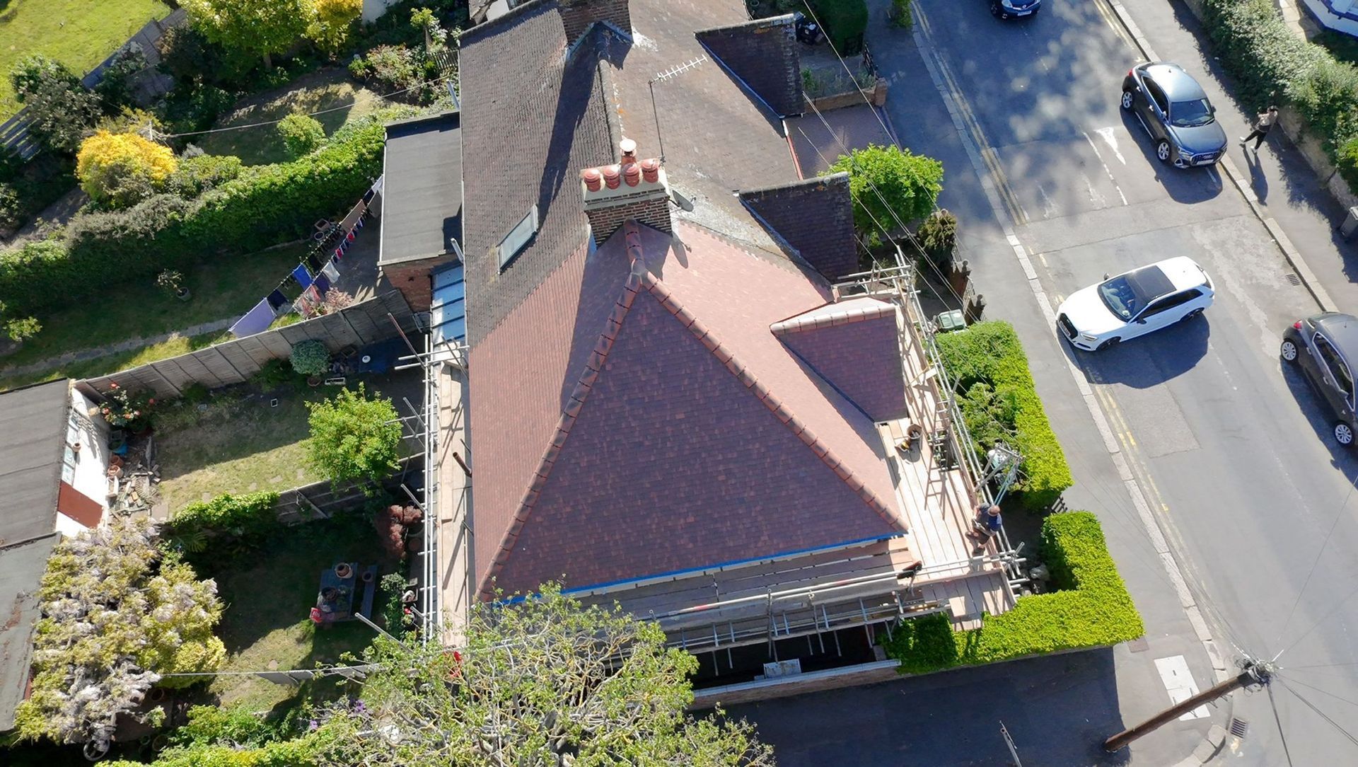 Aerial view of a red-roofed house beside a road with parked cars and trees.