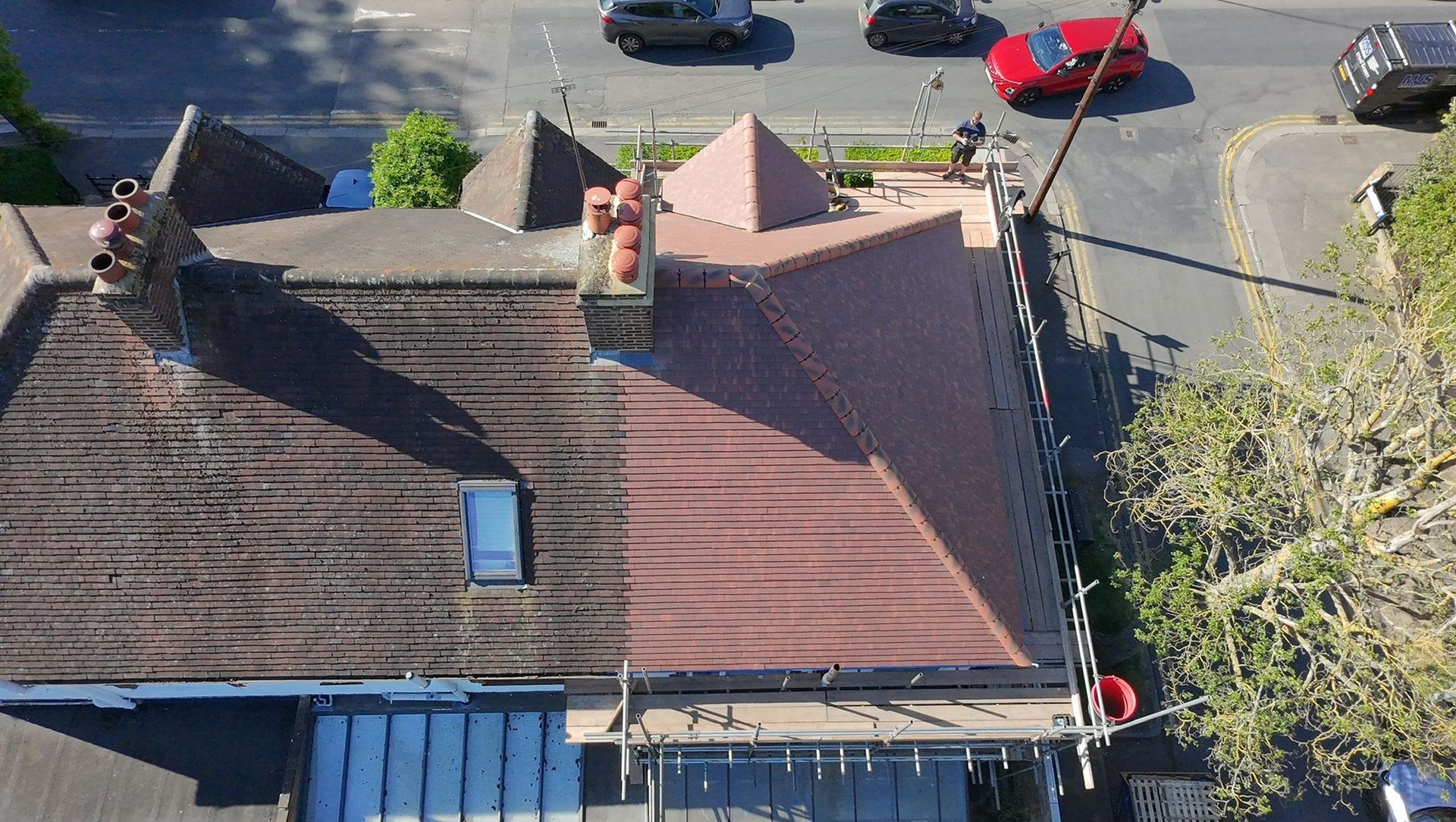 Aerial view of a house roof with chimneys, skylight, and a street with parked cars beside it