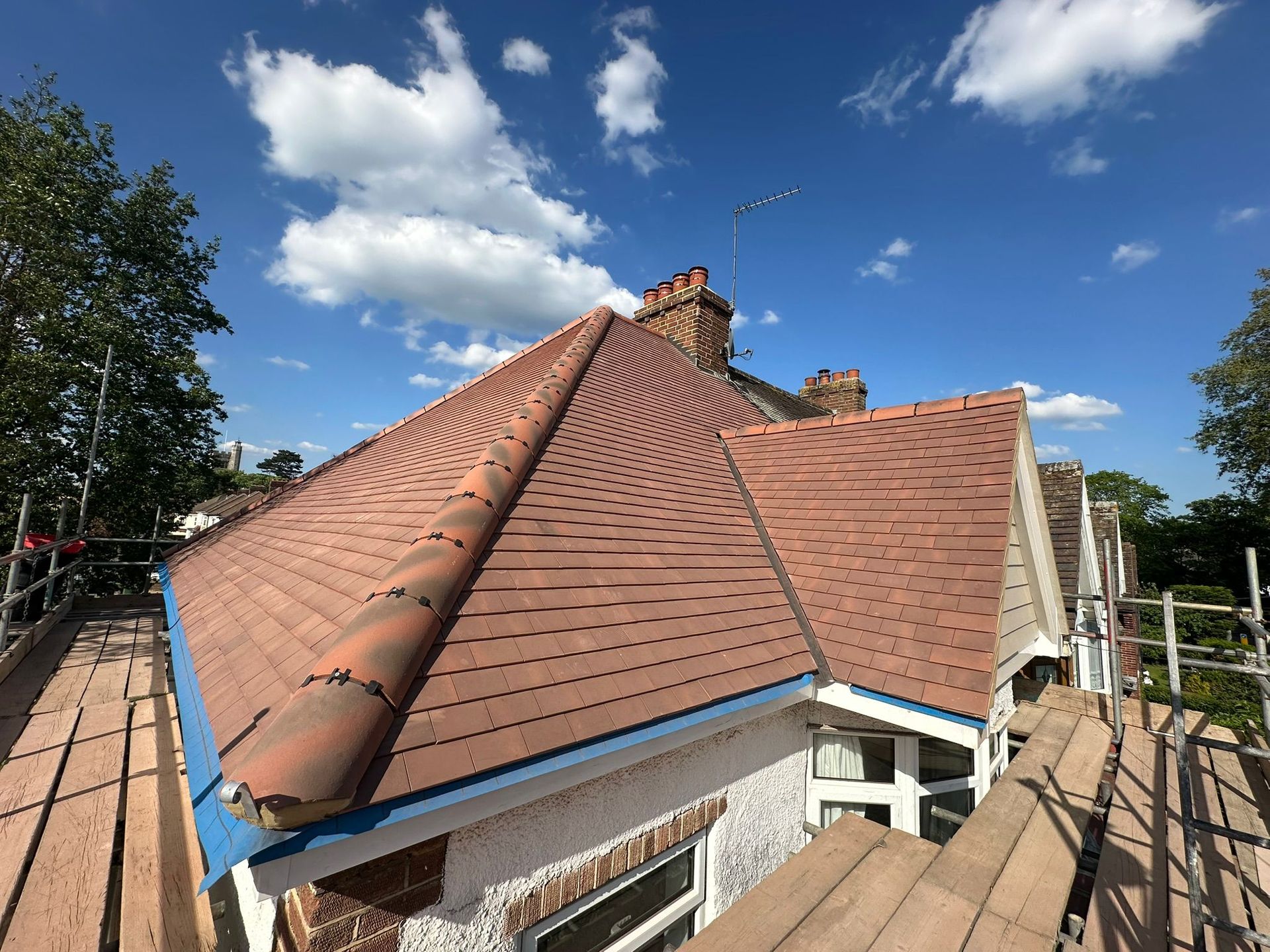 Red-tiled house roof under repair with scaffolding against a blue sky with clouds