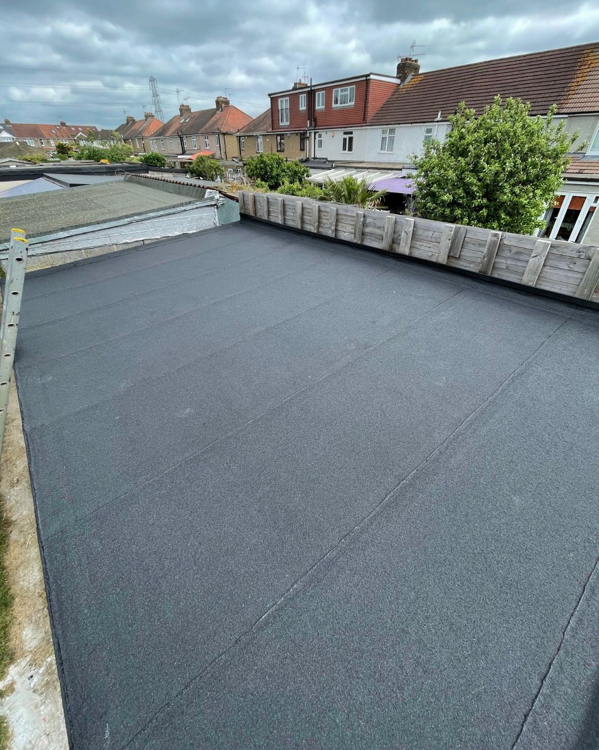 Newly installed flat, black asphalt roof with a low brick wall bordering the edges.