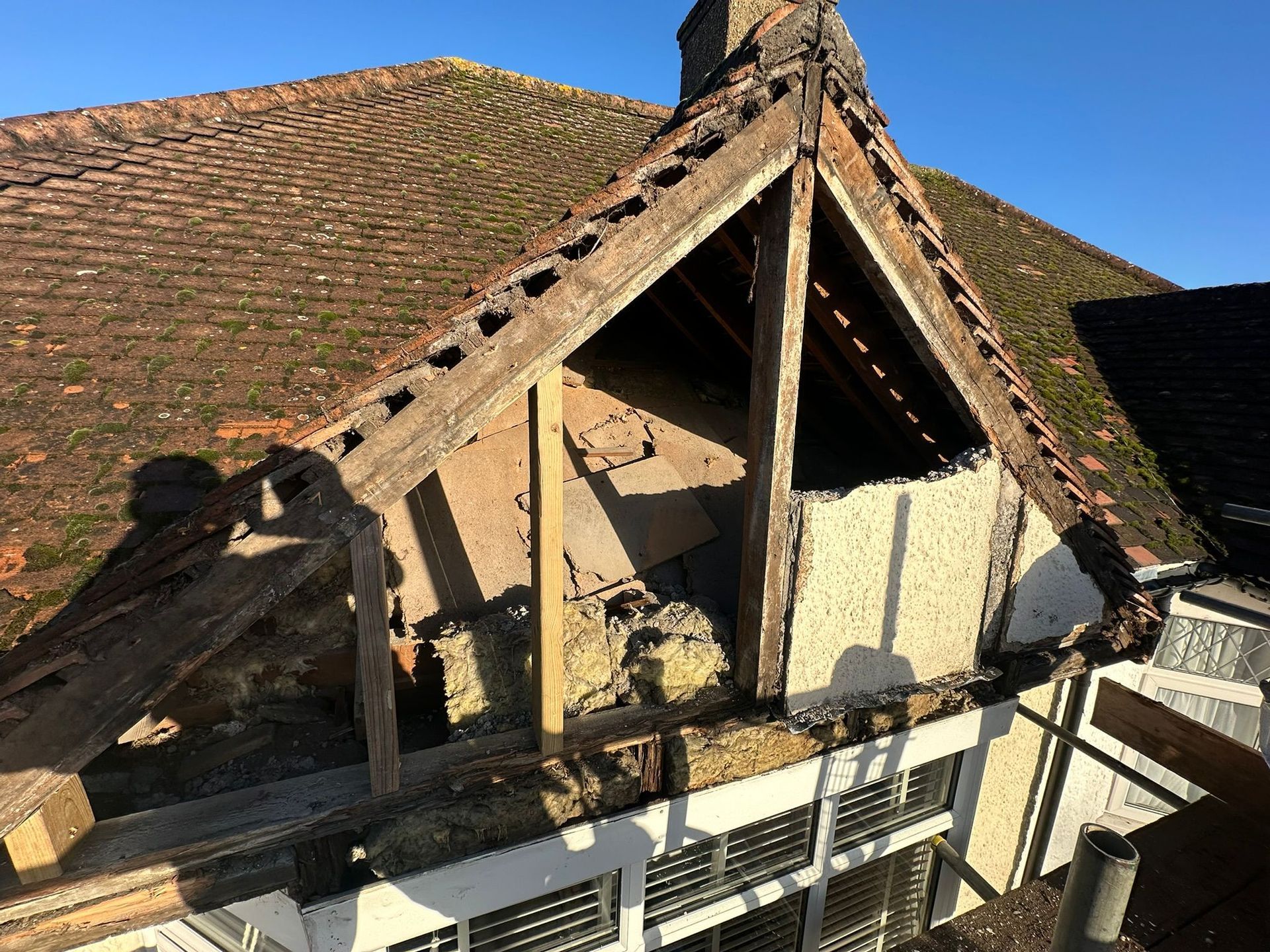 Damaged roof section with exposed wood and brick on a sunny day.