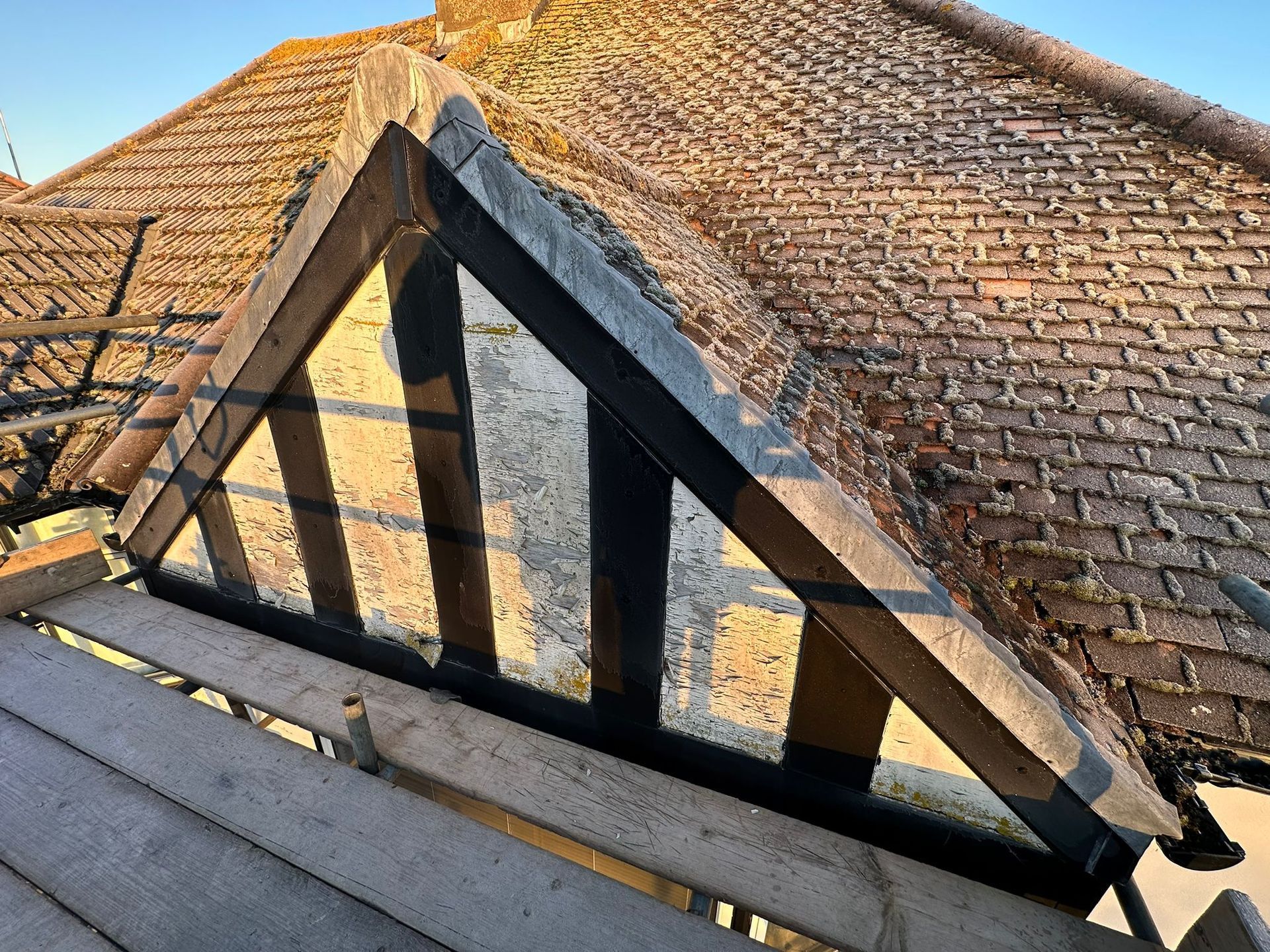 Wooden roof gable, dark painted beams, weathered brick tiles, sunlight.