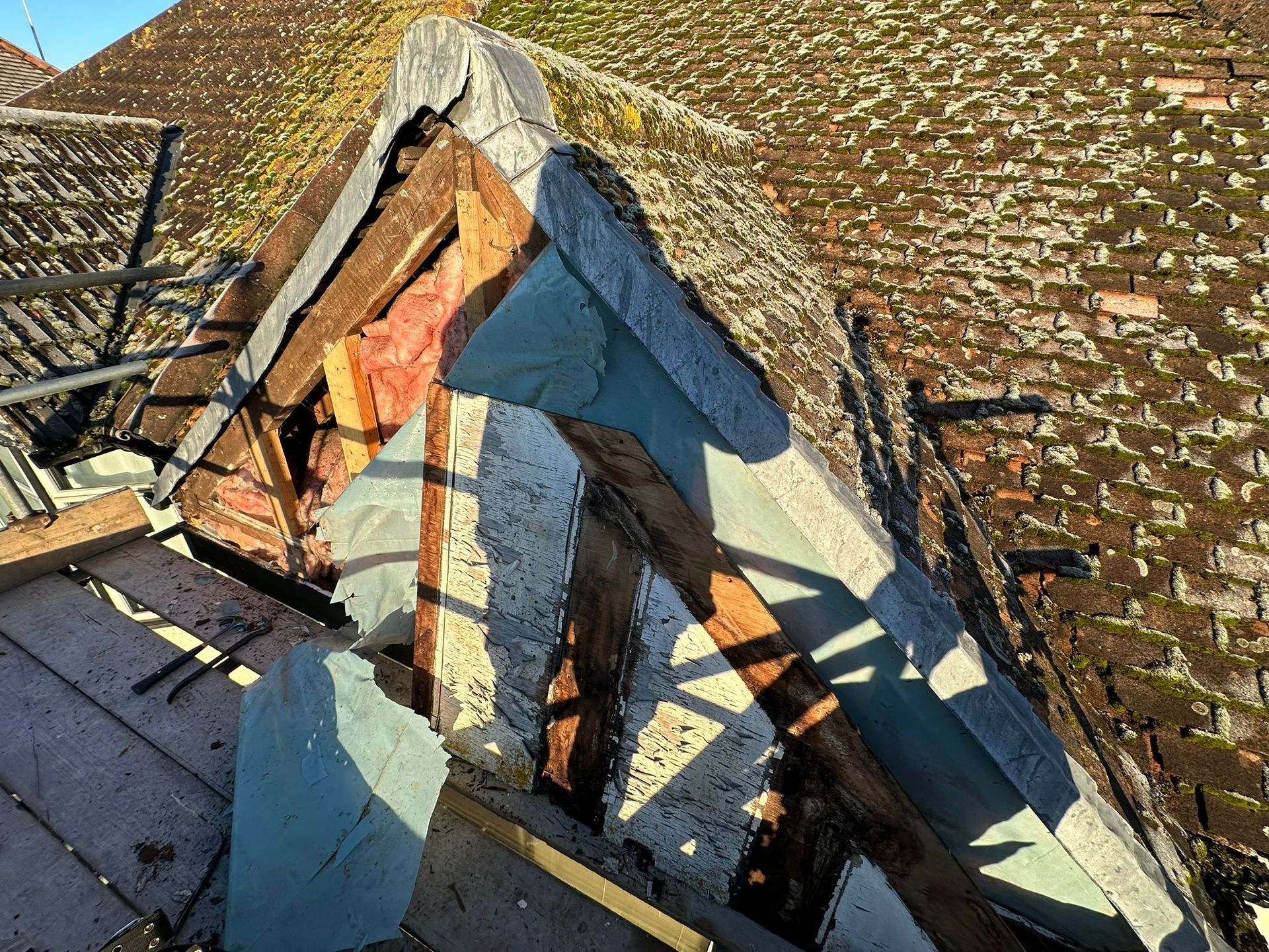 Damaged roof with missing tiles, exposed wood beams, and blue slate pieces.