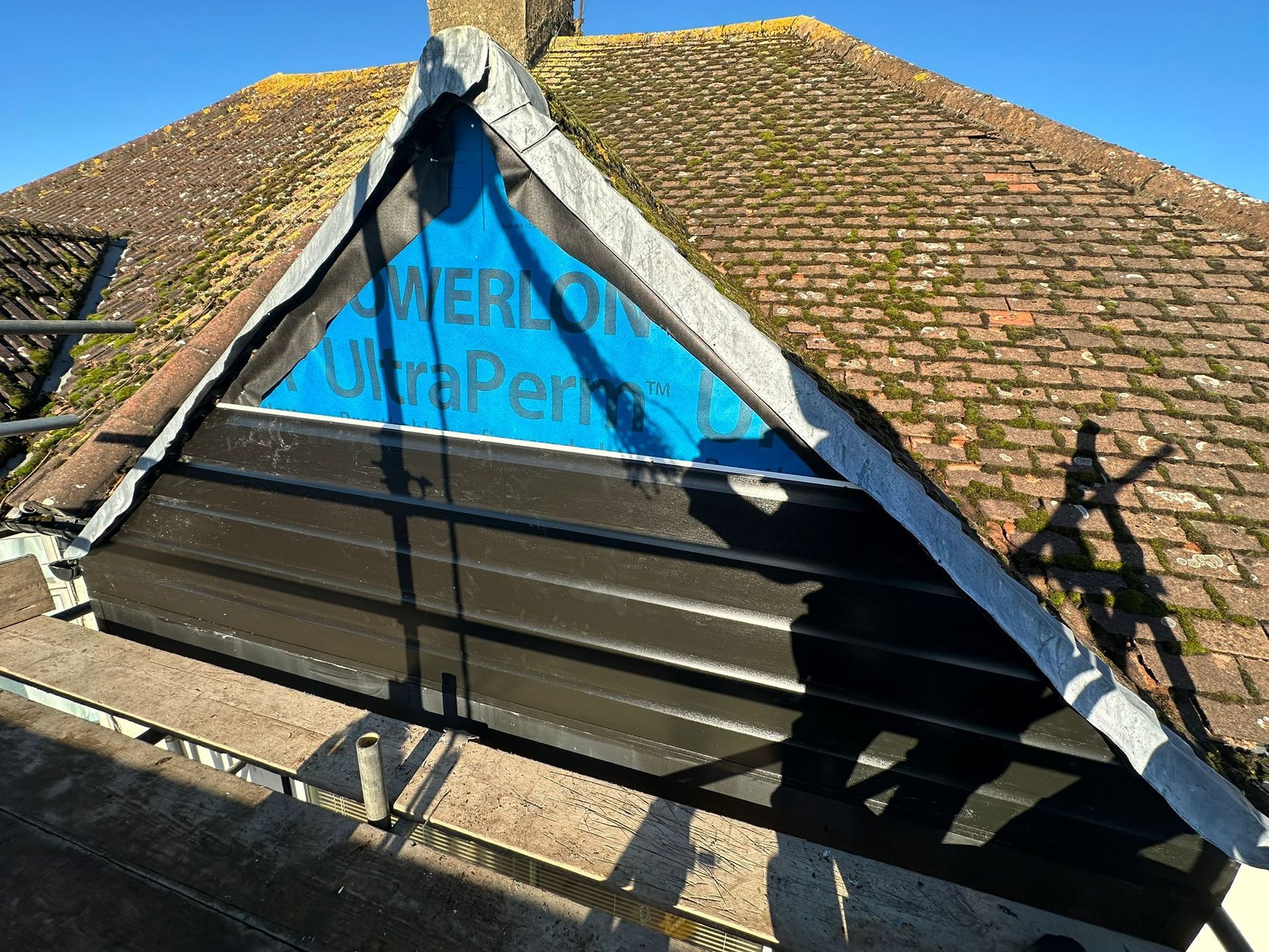 Roof repair: Black siding installed below blue underlayment on a gabled roof.