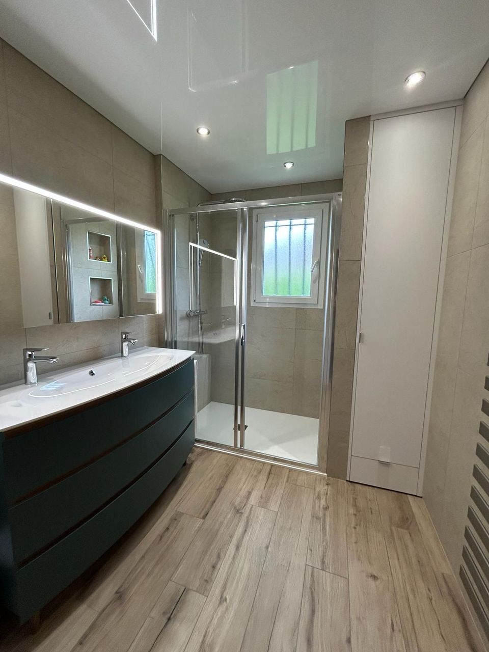 Salle de bain au Havre avec double vasque sur meuble bleu pétrole, douche à portes coulissantes et sol imitation parquet