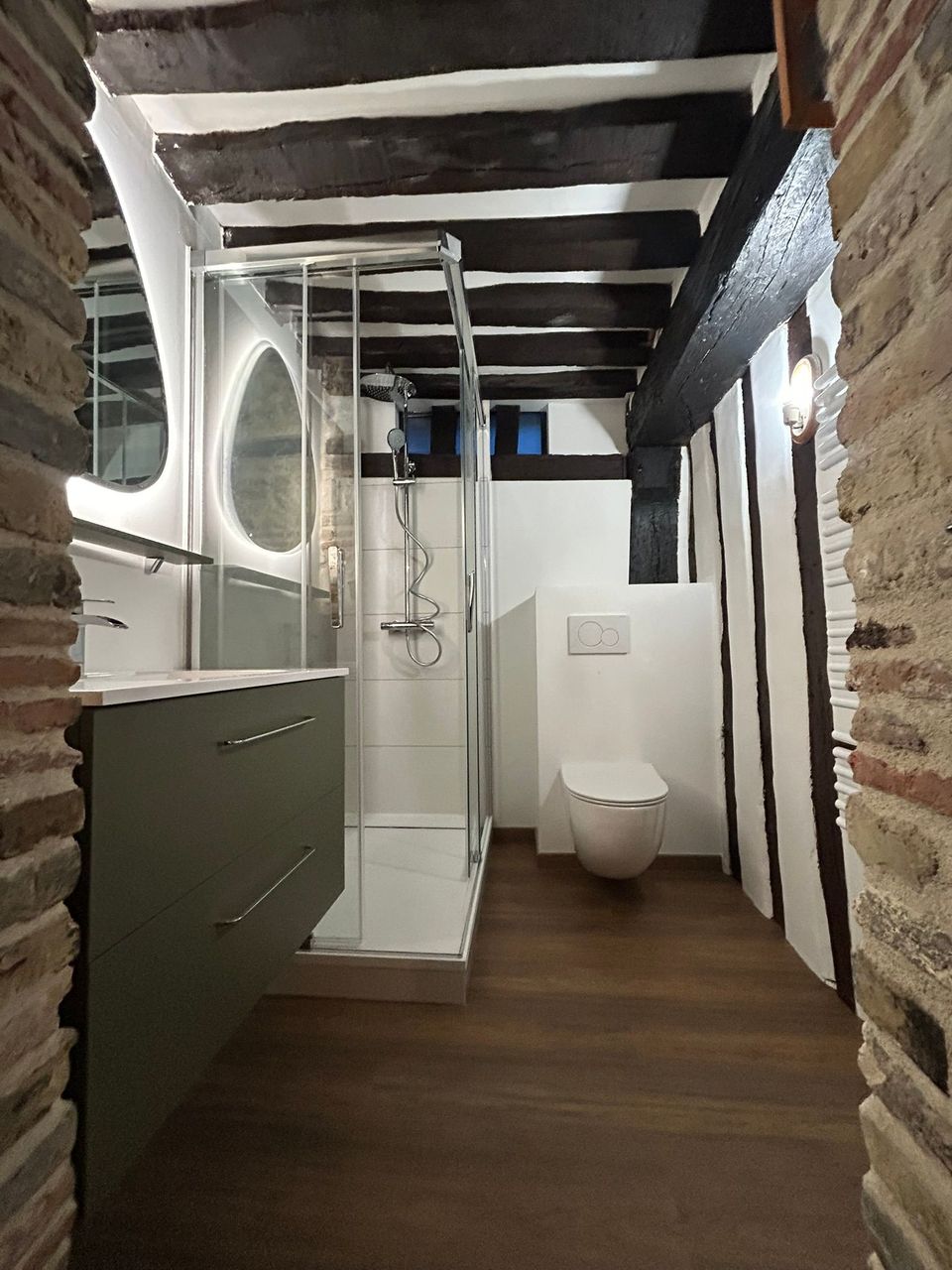 Rénovation de salle de bain au Havre dans une maison à colombages : poutres apparentes, meuble vert kaki, douche et WC suspendu