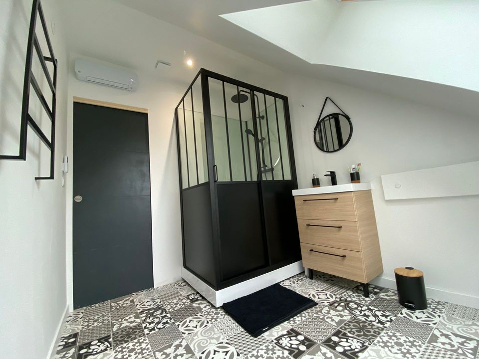 Salle de bain sous combles au Havre : douche style verrière noire et sol imitation carreaux de ciment