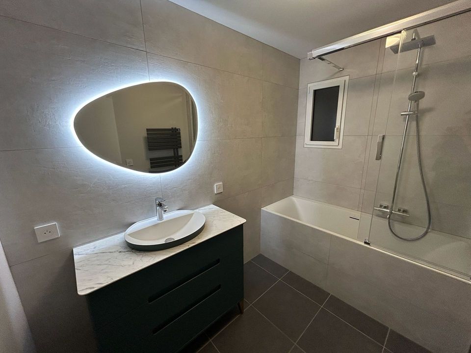 Salle de bain Milano au Havre : miroir galet rétroéclairé, vasque sur plan marbre et baignoire avec pare-bain