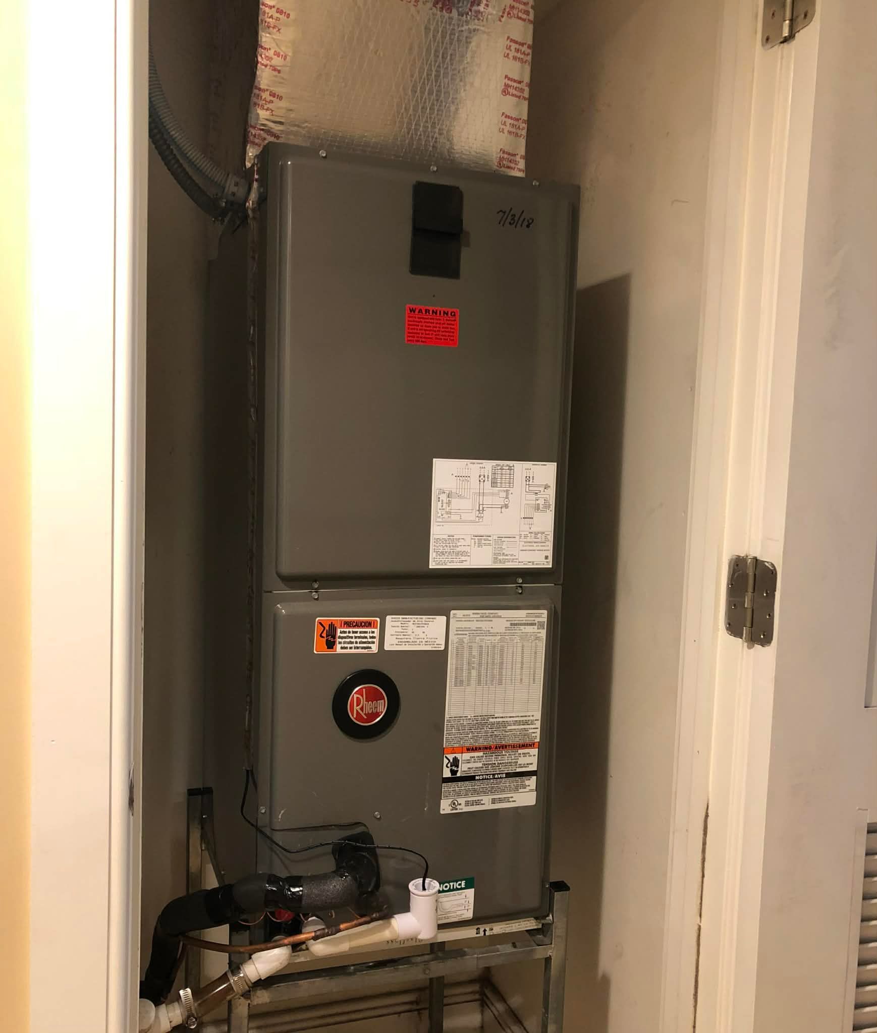 Gray HVAC furnace in a narrow utility closet with labels and visible ductwork above.