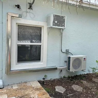 Exterior wall with windows, a utility meter, conduit, and an air-conditioning unit.