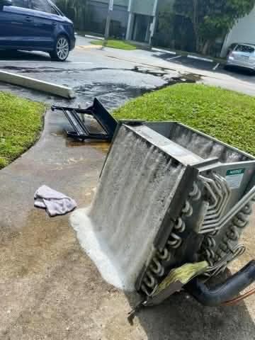 Overturned window air conditioner leaking water onto a sidewalk near a curb in a residential area