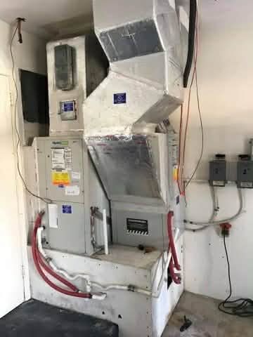 Wall-mounted HVAC ductwork and control panel with red hoses in an industrial utility room