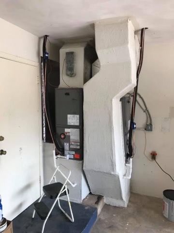 HVAC furnace in a utility closet with white insulation and attached pipes, next to a folding step stool
