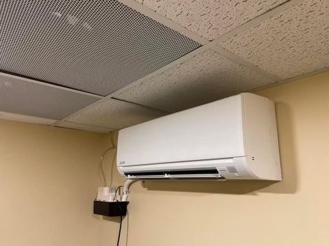 Wall-mounted outdoor air conditioner unit below a window beside a building exterior.
