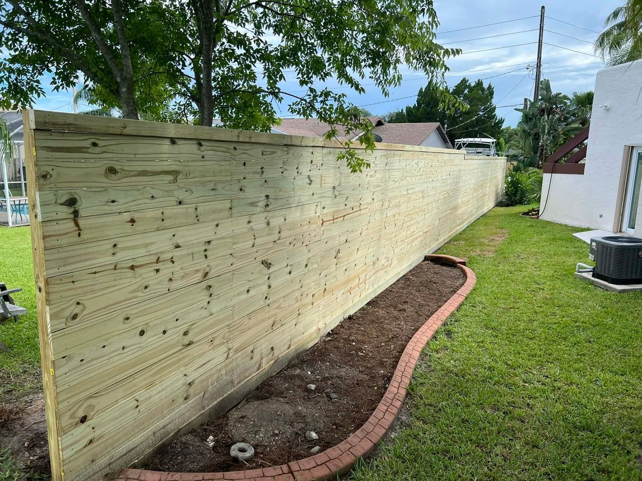 Long wooden fence along a narrow garden bed beside a lawn and house