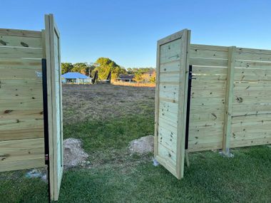 Open wooden gate leading to a grassy field at sunset