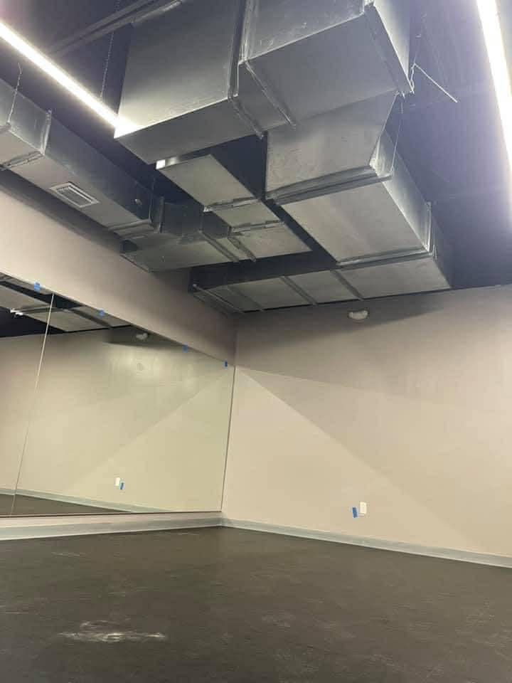 Empty room with exposed HVAC ductwork and mirrored wall panels on a dark floor.