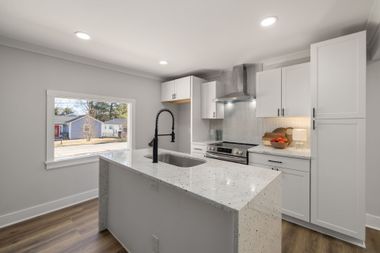 Bright modern kitchen with white cabinets, granite island, stainless appliances, and a window overlooking a yard