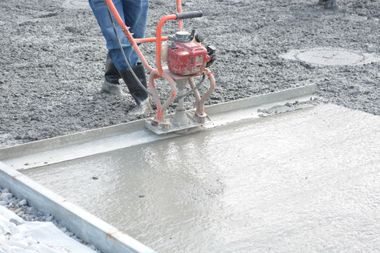 Worker using a red power trowel to smooth wet concrete on a slab