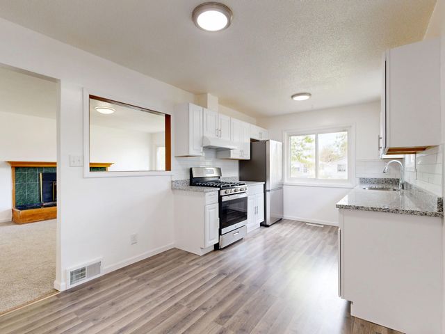 Bright white kitchen with wood-look floors, white cabinets, stainless stove, and a windowed dining nook.