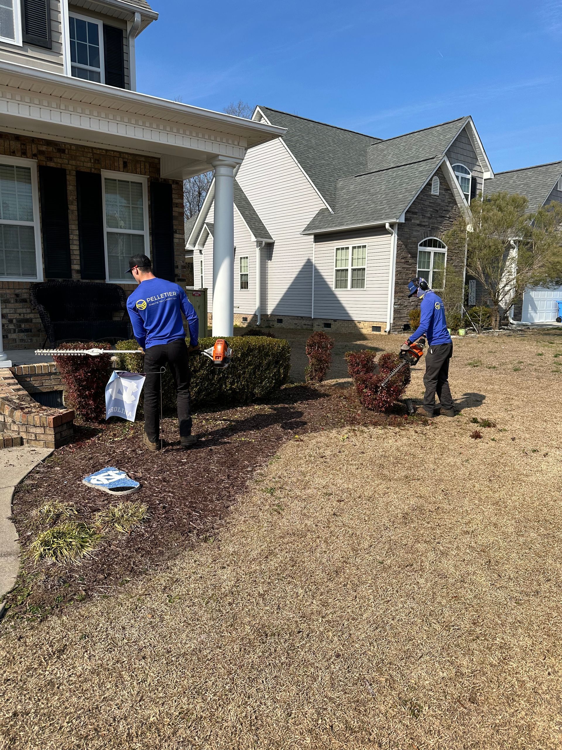 Two men are working in a yard in front of a house.