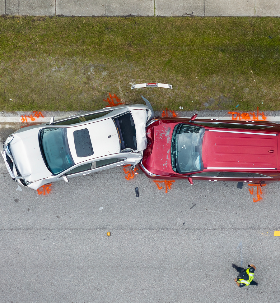 Overhead view of two crashed cars, red and silver, on a road, with a person in a safety vest nearby.