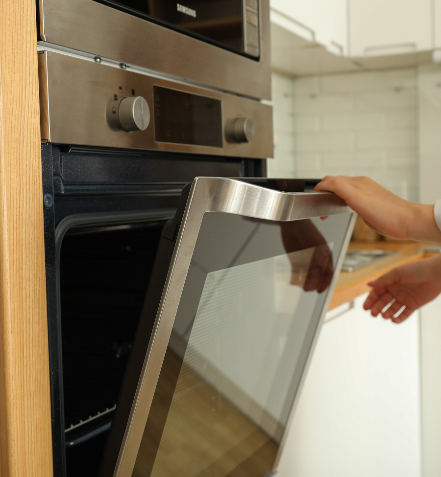 Person opening an oven door in a kitchen. Stainless steel oven, white cabinets.