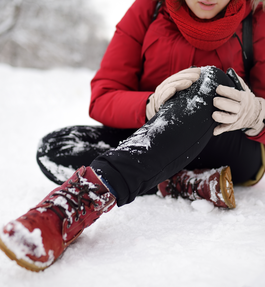 Person in red coat sitting in snow, holding knee, appearing to be in pain.