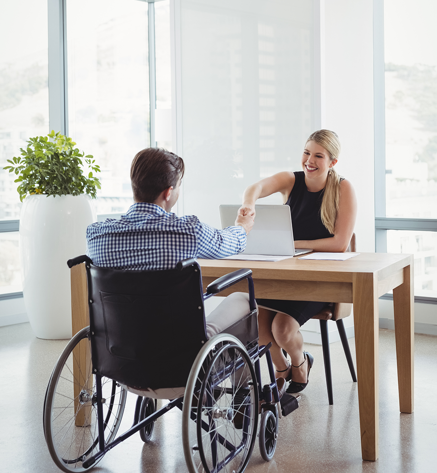 Person in wheelchair shaking hands with smiling person at desk. Office setting.