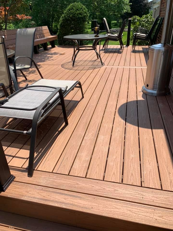 Wooden deck with outdoor furniture: lounge chair, table, chairs, and a heater. Trees in the background.