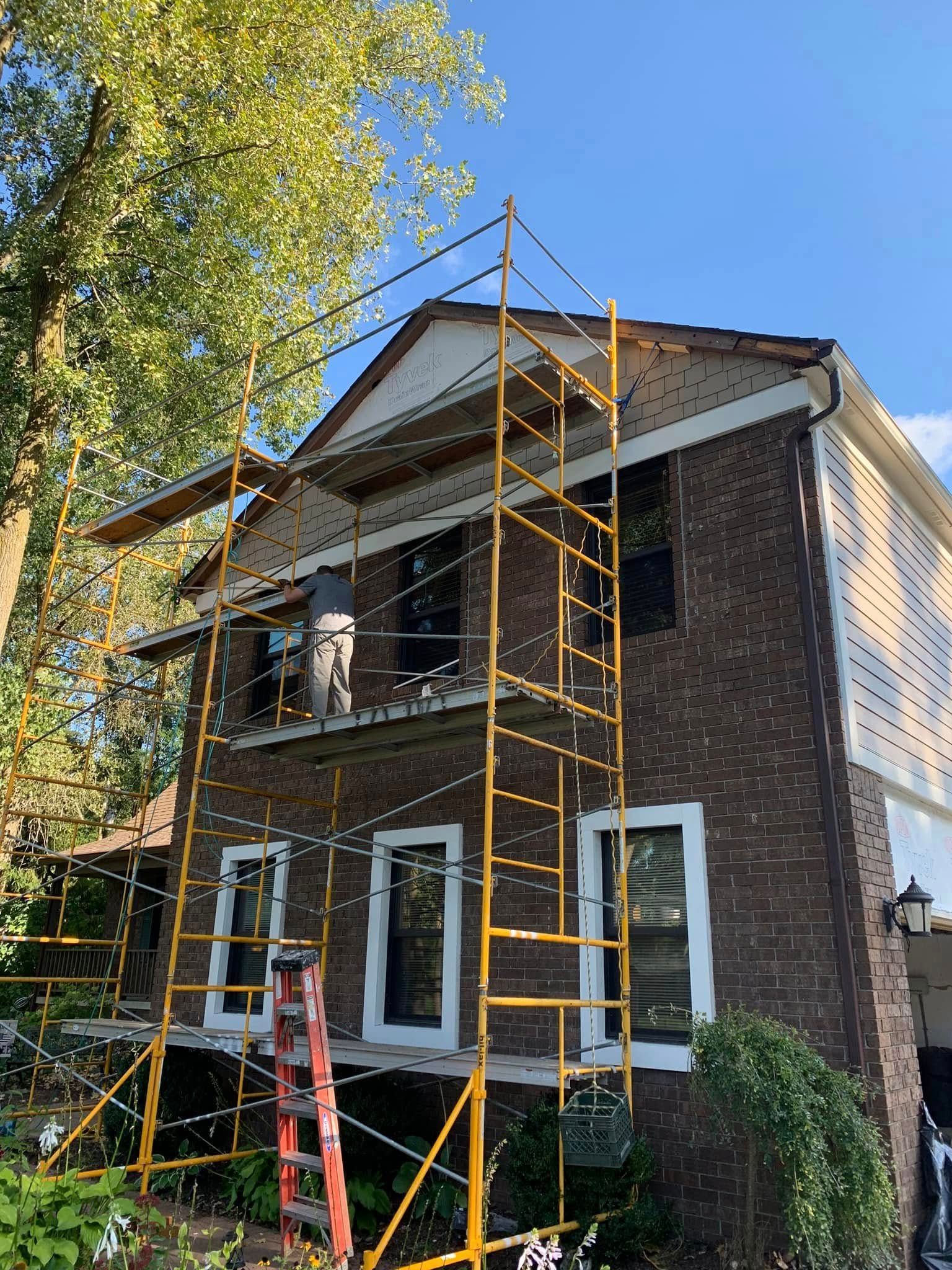Scaffolding against a two-story brick house during construction. A person is visible on the platform.