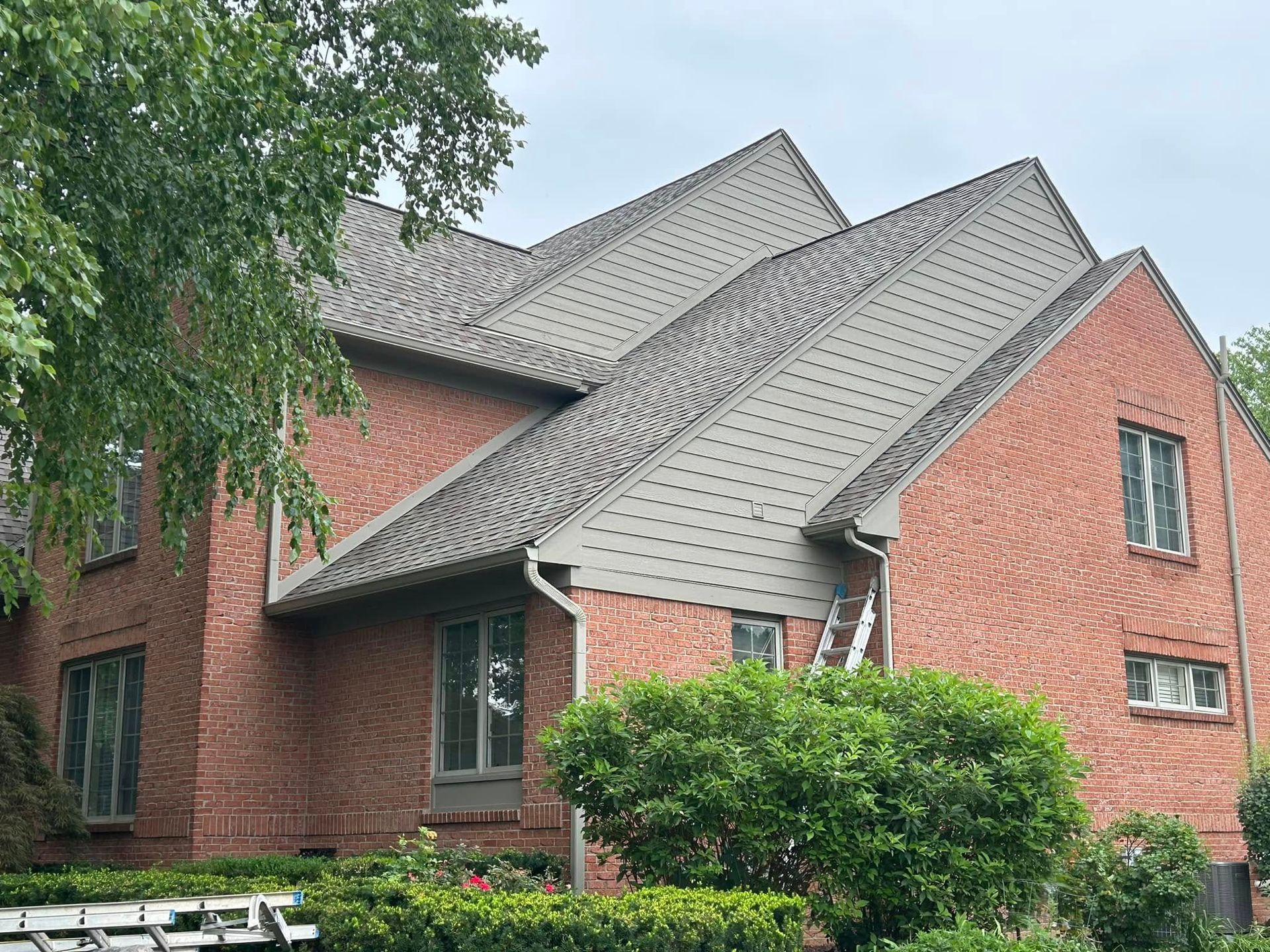 Brick house with gray roof, windows, and greenery.