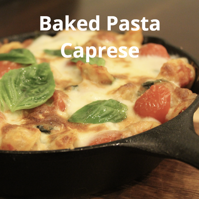 Baked Pasta Caprese, featuring penne or orecchiette pasta mixed with marinara sauce, cherry tomatoes, fresh basil leaves, and cubed mozzarella, topped with slices of fresh mozzarella and grated Parmesan cheese, broiled until golden and garnished with additional basil leaves.