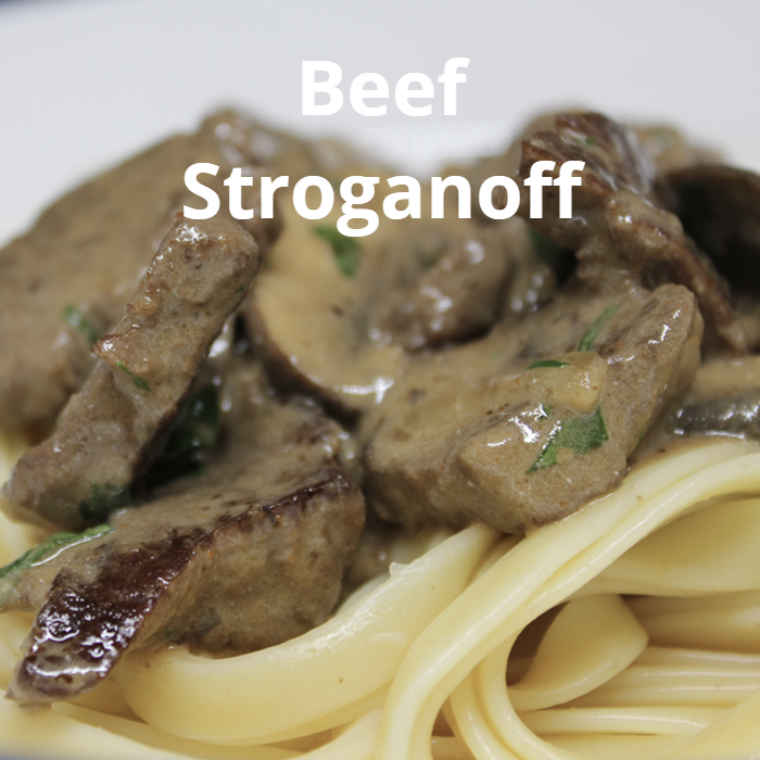 A hearty bowl of Beef Stroganoff, featuring tender cubed fillet steak, sautéed mushrooms, and onions in a creamy sauce made from beef broth, Dijon mustard, tomato paste, sweet paprika, and sour cream, served over buttered noodles.