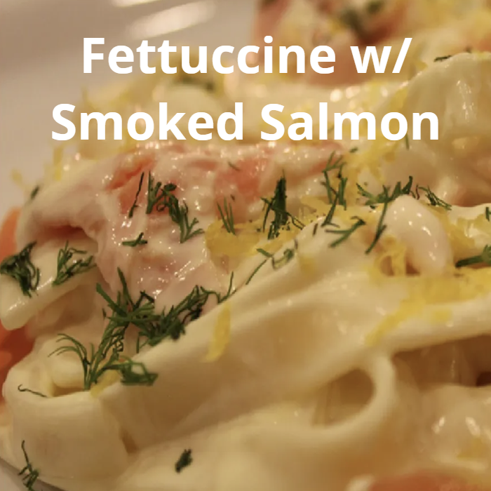 A delectable plate of fettuccine pasta topped with smoked salmon, mixed with a creamy sauce made from butter, cream, Parmesan cheese, garlic, sun-dried tomatoes, sautéed mushrooms, and spinach, garnished with freshly ground black pepper.
